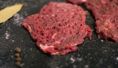 Raw pork chop with spices on a dark background.
