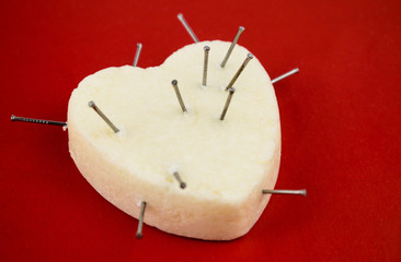The white heart is studded with nails on a red background. Concept of pain in the heart.