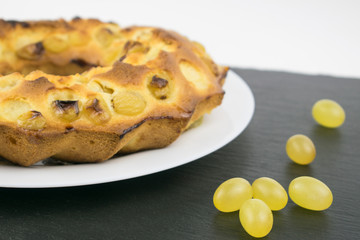 Pie with grapes on a white plate on a dark background.