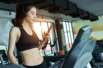 Asian woman exercising in the gym, Young woman workout in fitness for her healthy and office girl lifestyle. She using smart phone to check an email or social network.