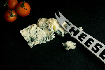 Cheese with mold and cherry tomatoes on a black background.