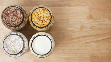 Various uncooked cereals, grains, and pasta for healthy cooking in glass jars on wooden table. Top view. Clean eating, balanced dieting food. Copy space.