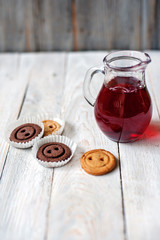 Jug with drink, cookies and a bouquet of flowers in a vase on a wooden background