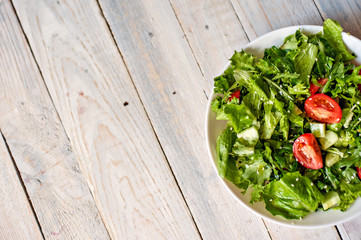 Salad from tomato, cucumbers, lettuce leaves and seeds of sesame on a white plate on a wooden background