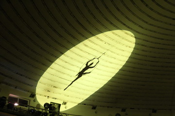 Shadow of gymnast of balancing actor performing number high above circus arena