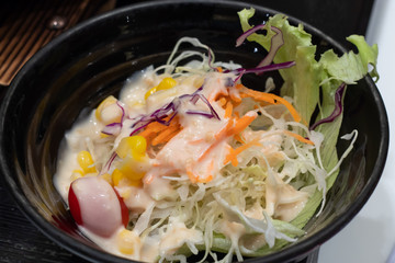 Vegetable salad in a black cup on the table.