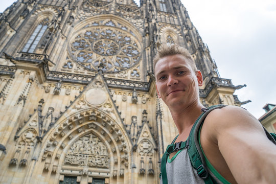 A young, handsome guy with blue crimson makes a selfi in the background of the St. Vitus Cathedral