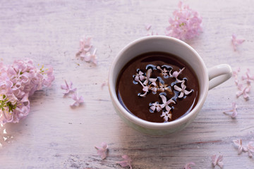 Purple lilac flowers and cup of tea on light wooden background/ teatime/ spring background/ cozy at home/ home spring decoration