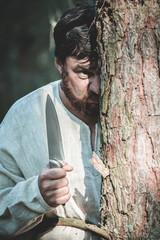 maniac with a knife stands behind a tree