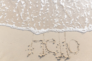 Fototapeta na wymiar The text Hello morning written on the sand beach by the sea, used in greeting