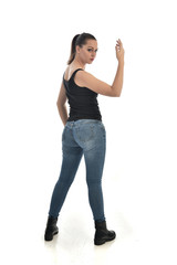 full length portrait of brunette girl wearing black single and jeans. standing pose with back to the camera. isolated on white studio background.