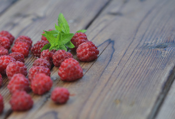 Late raspberry berries are covered with frost on a wooden background among them a sprig of mint