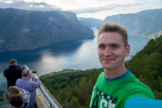 Young traveller taking selfie on the top with Beautiful fjord on background in Norway