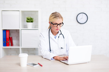 portrait of female doctor sitting in office and using laptop
