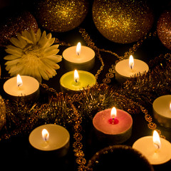 Burning candles surrounded by shiny balls and decor on a dark background.