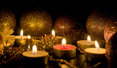 Burning candles surrounded by shiny balls and decor on a dark background.