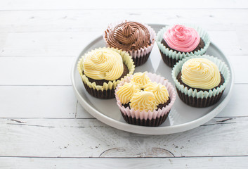 Frosted pastel cupcakes on white dish and wooden table