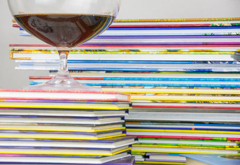 A stack of colorful books with a large glass.