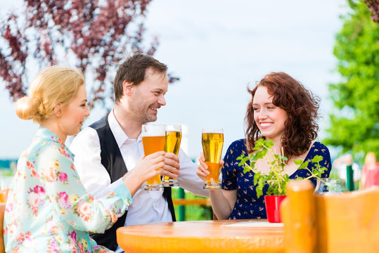 Happy friends toasting with beer in garden restaurant