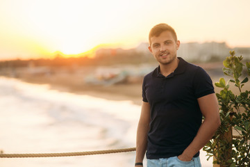 handsome man standing on pier near the sea in sunset time