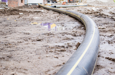A large polyethylene pipe for gas lies on the mud near the house under construction.