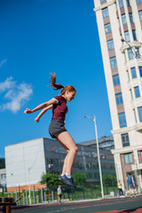 the red-haired student in shorts gives the standards for jumping at the physical education class on an open sports ground. girl doing crossfit exercises outdoor. red-haired young woman is jumping