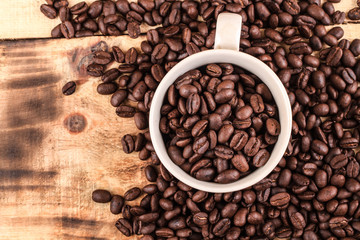 Cup of coffee full of coffee beans on wood background, top view