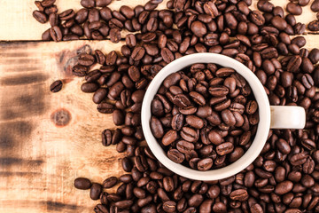 Cup of coffee full of coffee beans on wood background