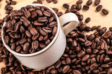 Cup of coffee full of coffee beans on wood background, side view