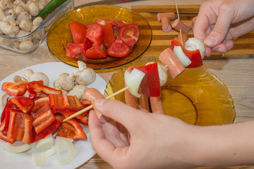 Preparing shashlik for barbecue grill. A hand puts pieces of Champignon, sausages, tomatoes, pepper...