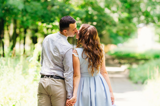 guy and girl stand back to the camera holding hands and kissing on the background of the park