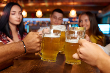 Four friends toasting with glasses of light beer at pub.