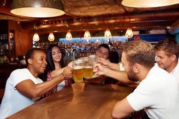 Group of happy friends enjoying beer at pub, toasting and laughing.