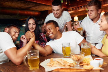 Two playful male friends having arm wrestling challenge at bar.