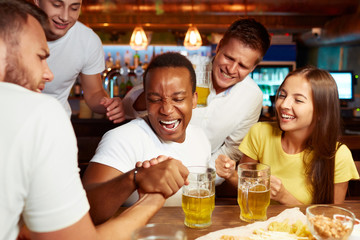 Excited male friends having arm wrestling challenge at local bar.