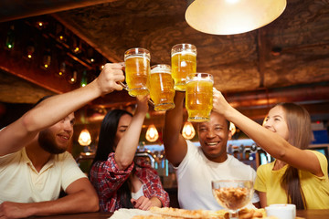 People raising beer glasses high above table and looking on drink.