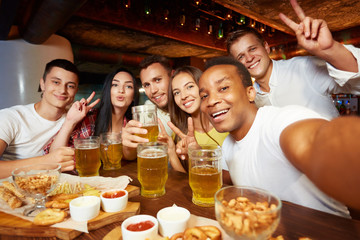 Company of happy friends taking self portrait with peace sign gesture.