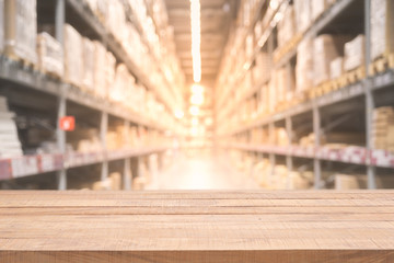 Empty wooden table on defocused blurred boxes on rows of shelves in warm light warehouse background...