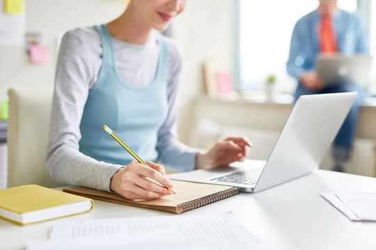 Close-up of girl sitting at table and using laptop while summarizing online article at class