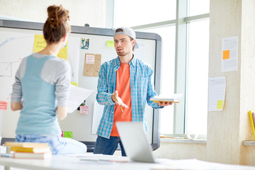 Obraz premium Serious pensive handsome guy in cap and casual shirt gesturing while arguing with colleague in office, they brainstorming about marketing plan
