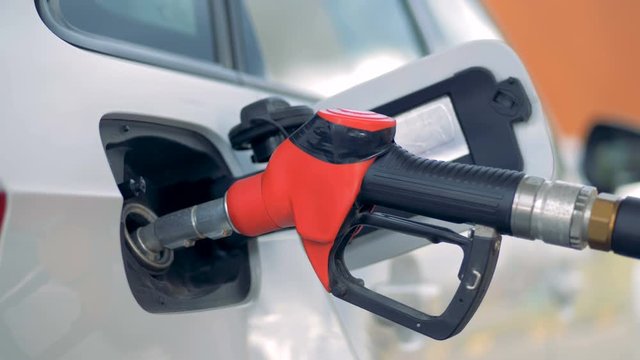 A red gas nozzle in a car tank, close up.