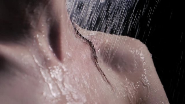 Brunette woman taking a shower. Wet hair lie on the beautiful naked shoulders and close up neck in water drops. Shower rain falling down. Sensual and seductive concept, lady enjoy shower in bath room