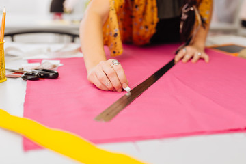 Holding chalk. Careful attentive dressmaker putting her hands on the pink fabric while being in the atelier and drawing the lines