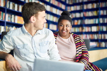 Cheerful African female student talking with her friend at library