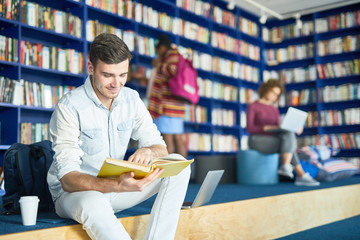 Young male student sitting with coffee and book at college library, he is preparing for exam
