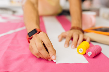 Hand with chalk. Close up of a person drawing the line on pink textile while having pink and yellow bobbins by his side