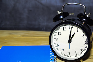 concept vintage background black retro alarm clock on 13.00 pm or 01.00 am and blue book
