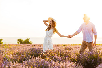 Cute loving couple walking in the lavender field outdoors holding hands of each other.