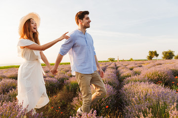 Photo of joyful young couple man and woman dating, and walking outdoor in lavender field