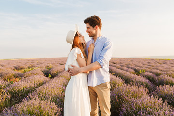 Photo of loving couple young man and woman hugging, while walking outdoor in lavender field